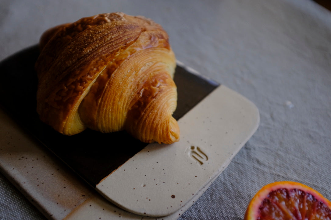 Planche Aimée, conçue pour les petits-déjeuners, l'apéro ou peut être utilisée comme dessous-de plat. Bi-matière : émail noir effet et grès belge moucheté. Émail brillant. Entretien : Lave-vaisselle. Dimensions : l.13,5 x L.20,5 cm